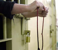 An Iraqi female prisoner works prayer beads through cell bars at Abu Ghraib Prison